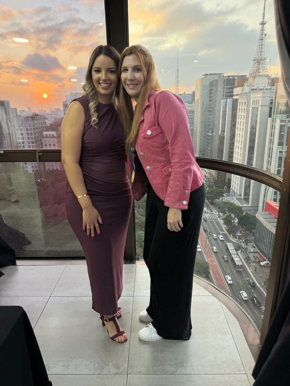 Stefany e uma participante posam no fim de tarde, com a cidade ao fundo, na edição de 2025