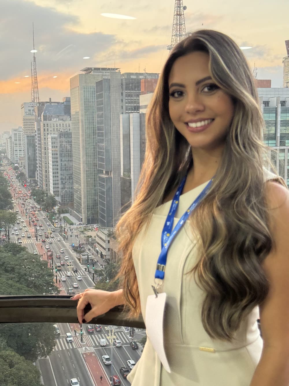 Participante de crachá sorrindo, com a Avenida Paulista ao fundo, na edição de 2025